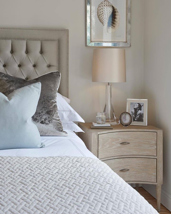 Taupe tufted headboard with gray pillows, a pale blue accent pillow, and a textured light coverlet.