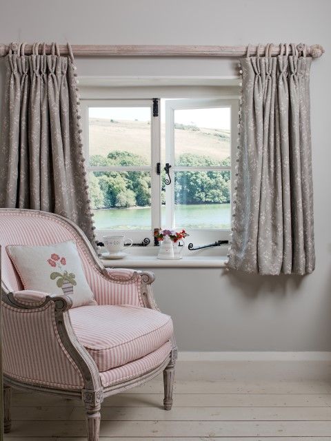 Short gray patterned curtains around a small window beside a pink striped armchair.
