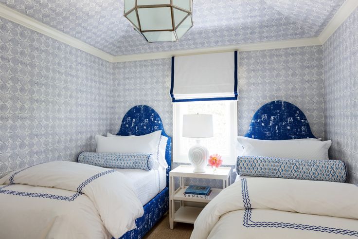 Two blue curved headboards with white bedding, blue trim, and patterned bolster pillows.