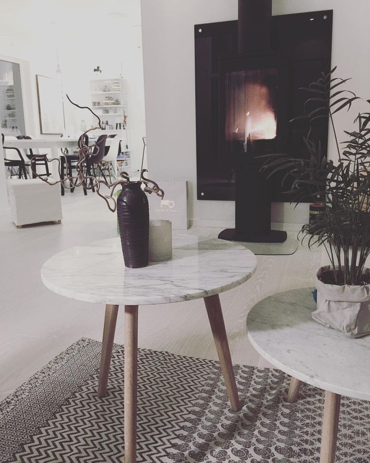 A black fireplace behind pale round tables, with a black-and-white patterned rug below.