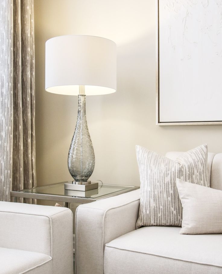Cream seating with beige pillows, a glass side table, and a shaded table lamp.