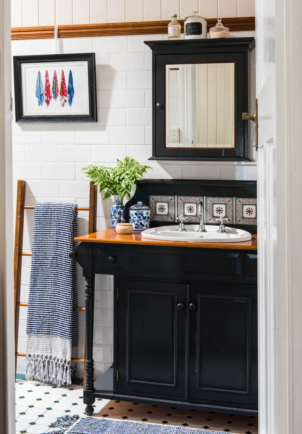 A blue and white towel hangs on a wooden ladder beside a dark vanity with blue and white containers.