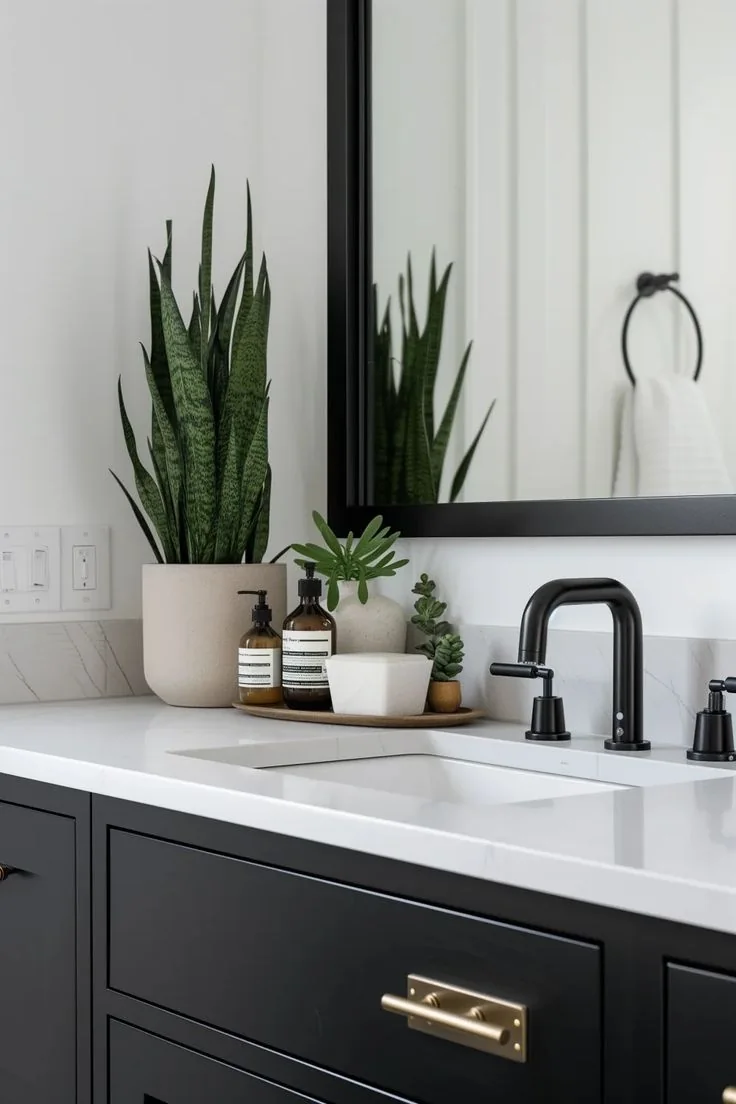 A narrow oval tray holds two amber bottles and small white planters beside a black bathroom faucet.