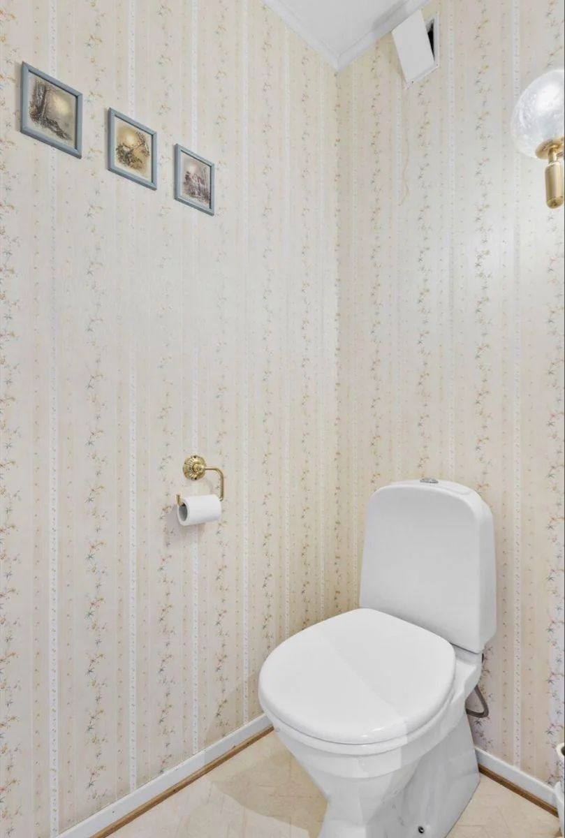 Three small blue-gray picture frames hang in a row on pale floral striped wallpaper beside a white toilet.