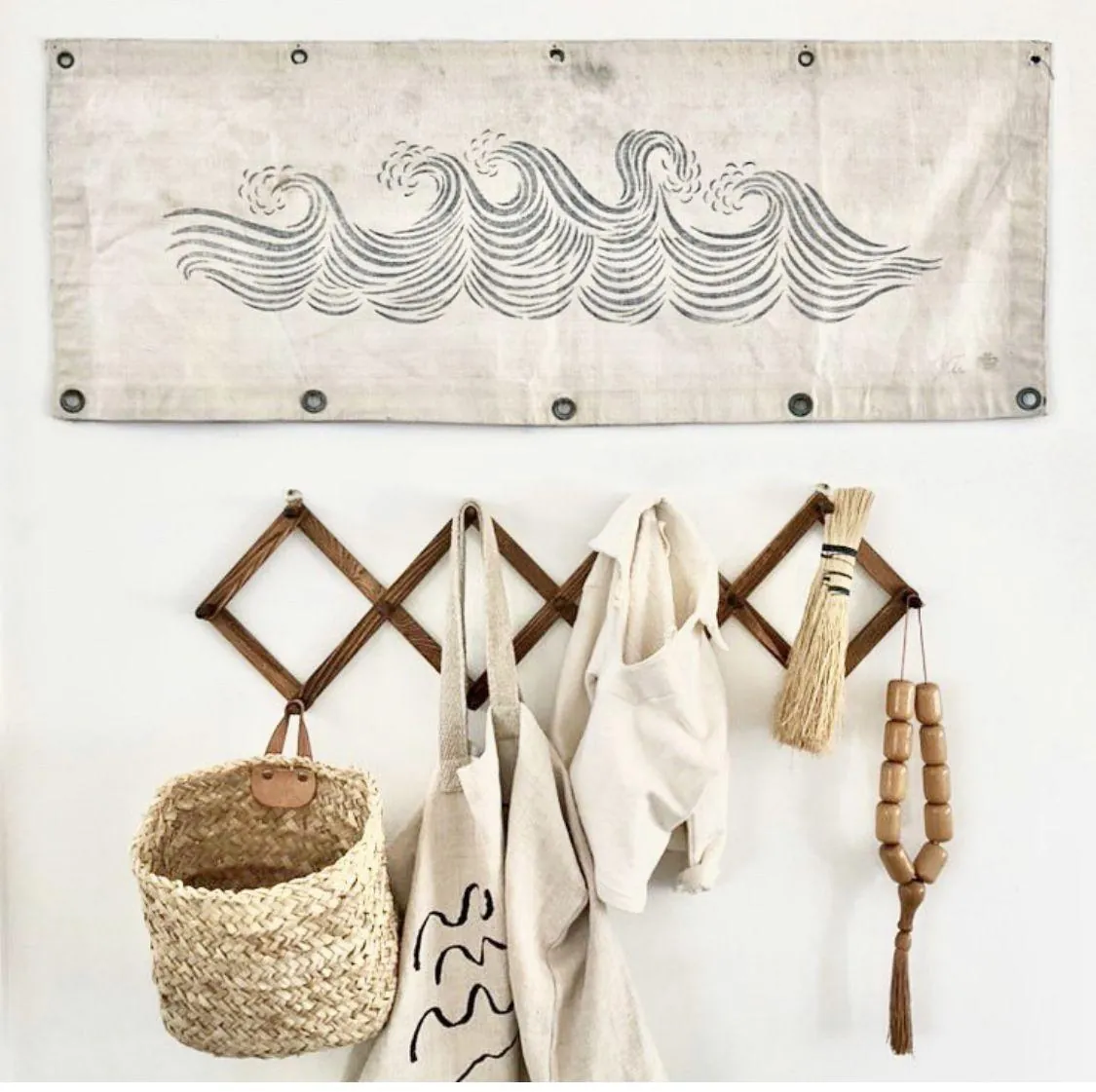 A pale fabric hanging with dark wave lines sits above a wooden accordion rack holding a basket, cloths, and brushes.