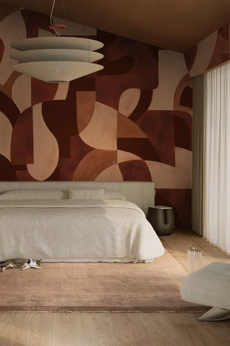 A large abstract wall pattern in brown and cream sits behind a pale upholstered bed.