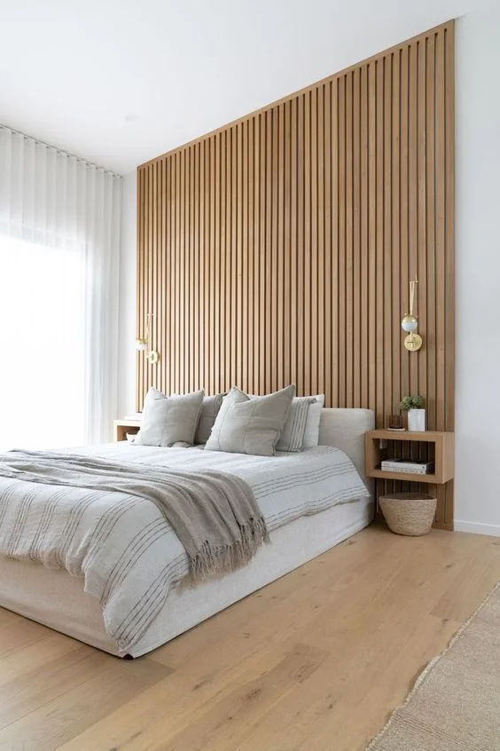 A full-height vertical slat accent wall stands behind pale bedding and two hanging bedside lights.