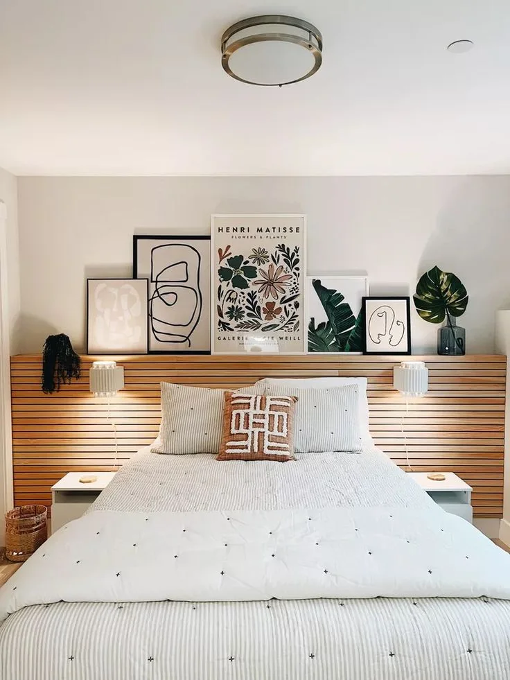 A horizontal slat accent panel sits behind a white bed with framed prints arranged along its top edge.