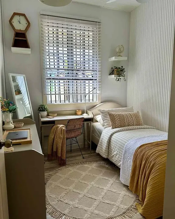 A small adjustable lamp stands on a desk beside a bed.