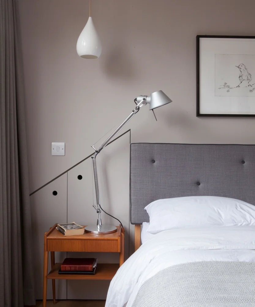 An adjustable silver table lamp stands beside a gray bed beneath a white pendant.