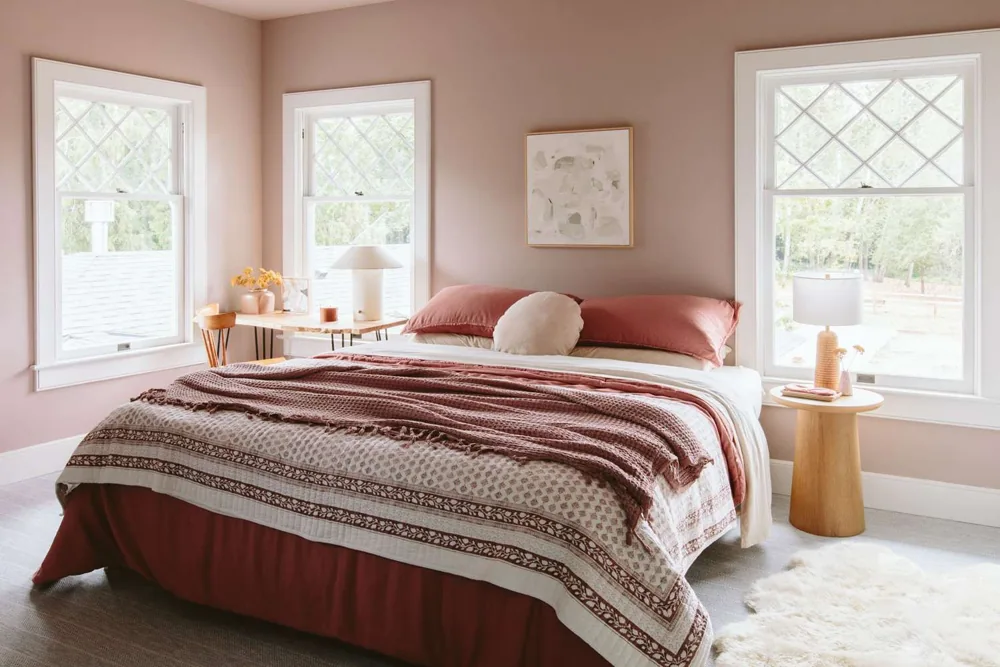 A pale rug extends beside a bed with pink bedding in a soft pink room.