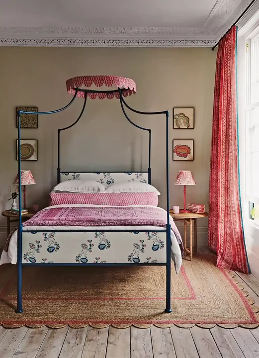 A tan rug with a pink border frames a blue metal bed with patterned pink bedding.
