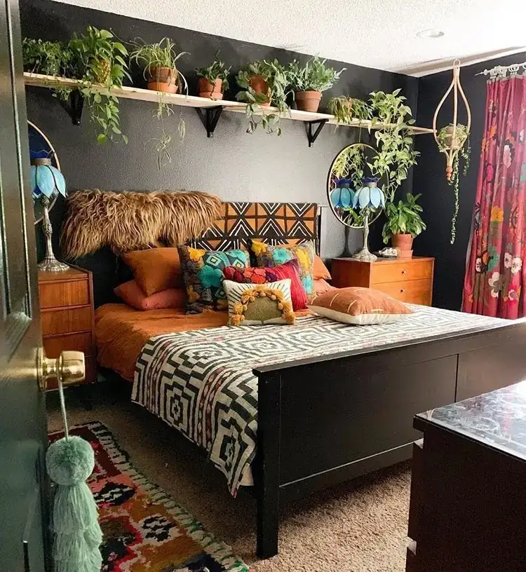 A dark-walled bedroom has a high plant shelf, orange bedding and a patterned headboard.