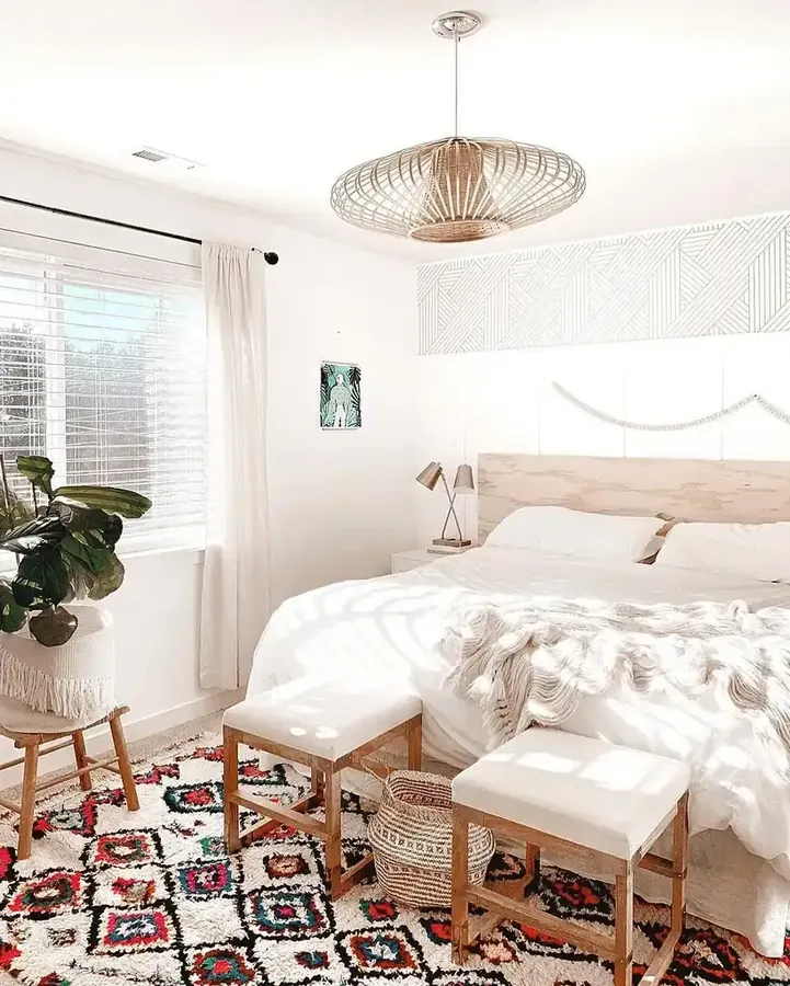 A white bedroom pairs a woven pendant with a colorful patterned rug and two stools.