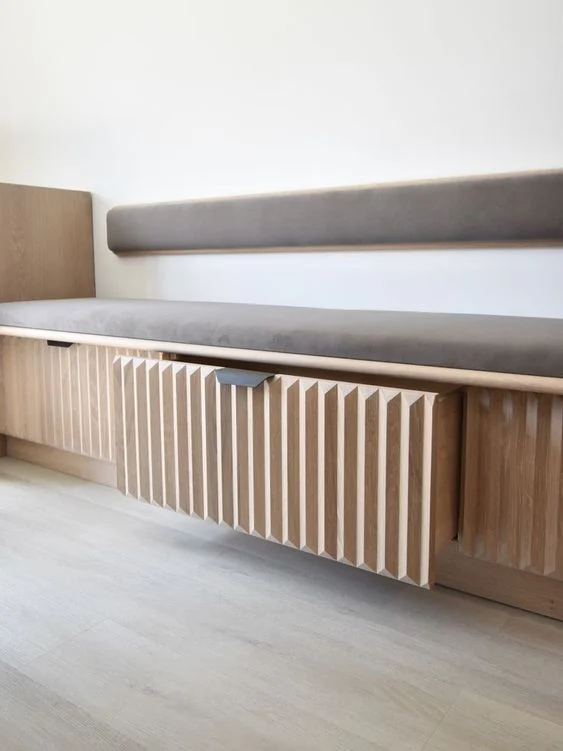 A gray cushioned bench has a narrow wall backrest and a wood-toned slatted front.