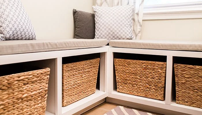 Woven baskets fill open cubbies beneath a pale corner bench with neutral cushions.