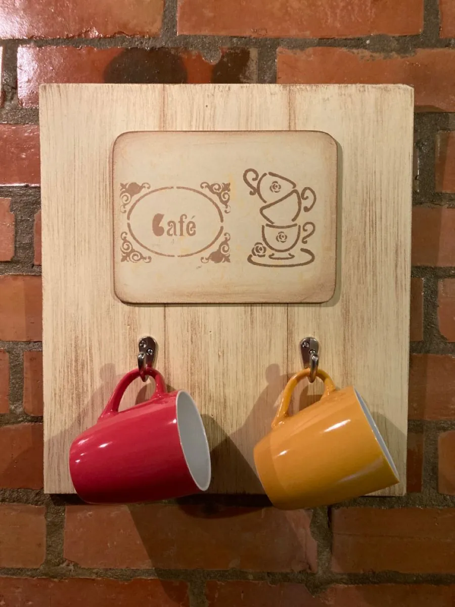 Red and yellow mugs hang from hooks on a wood-toned café panel against a brick wall