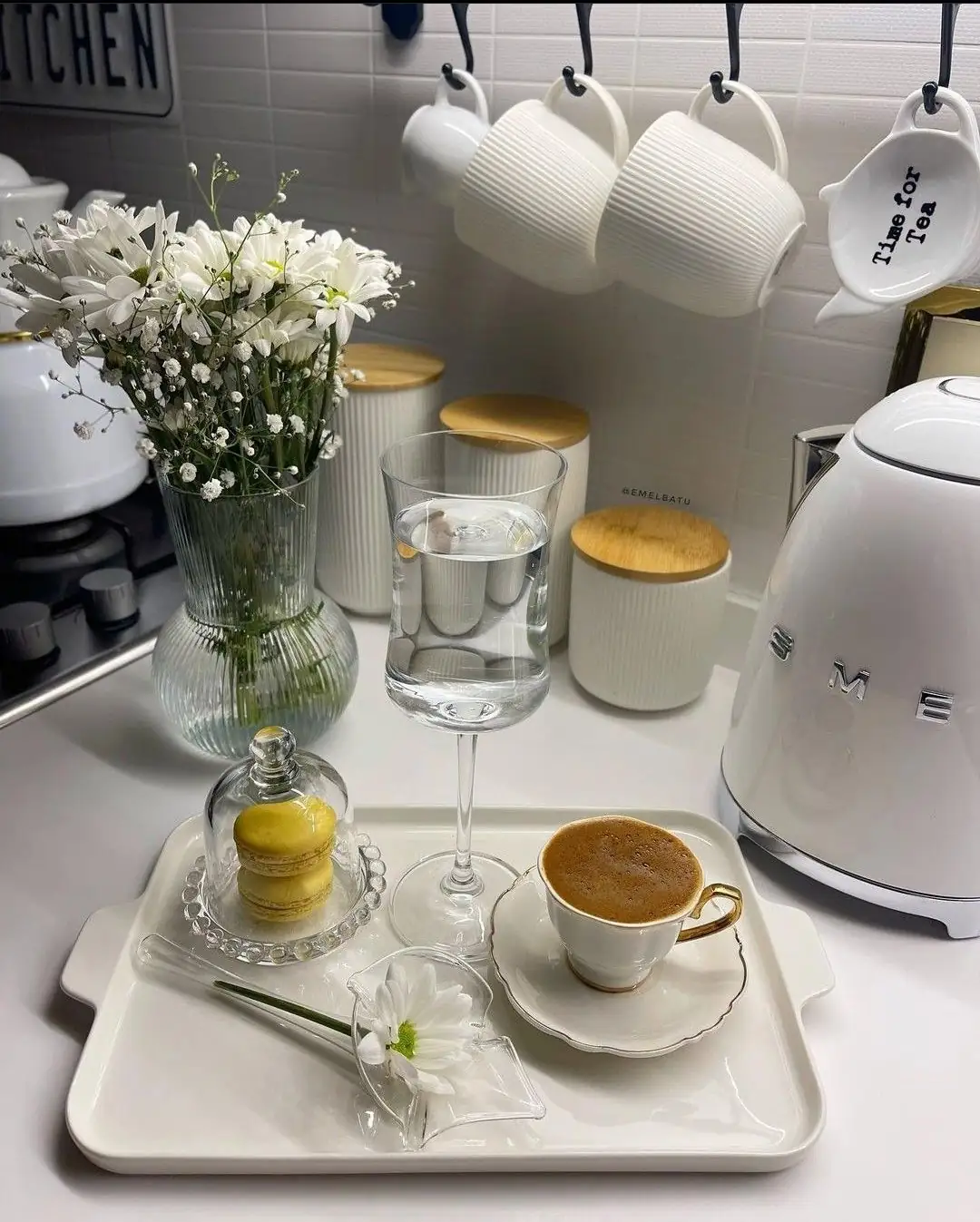 A white tray holds a coffee cup, a stemmed glass, and small accents beneath hanging white mugs