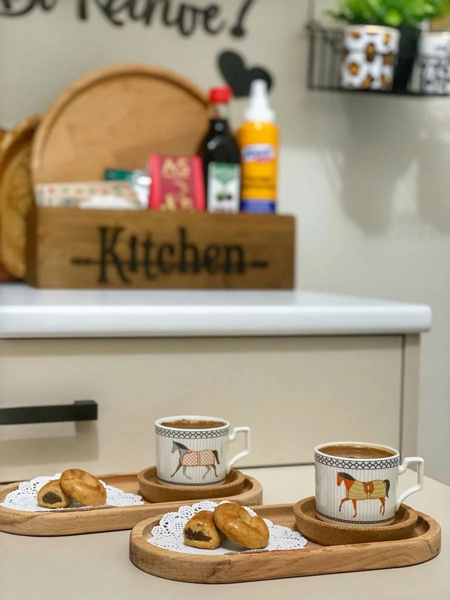Patterned coffee cups and small pastries sit on separate wood-toned trays on a kitchen counter