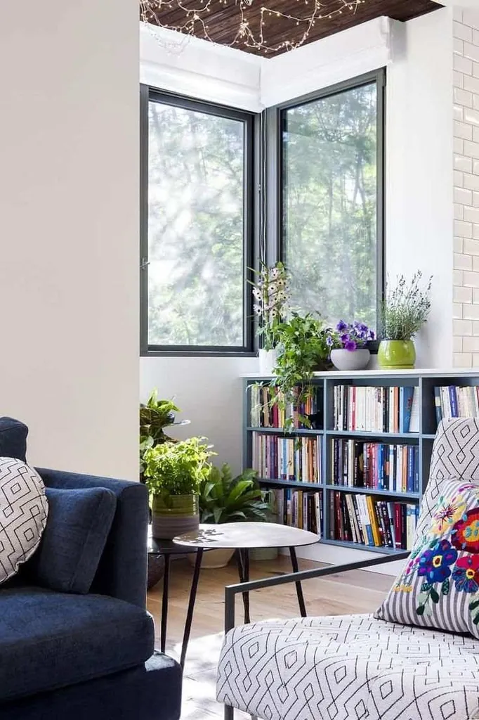 A navy sofa and geometric-patterned chair beside a low bookcase and corner windows.