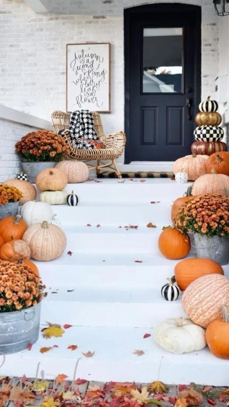 Pumpkins and rust-colored flowers along the edges of white porch steps leading to a dark front door