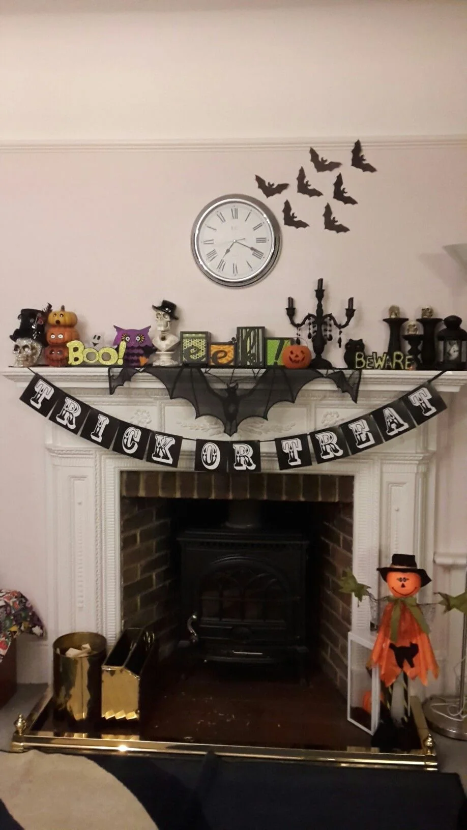 Black bats beside a round clock above a white mantel with colorful Halloween ornaments and a Trick or Treat banner