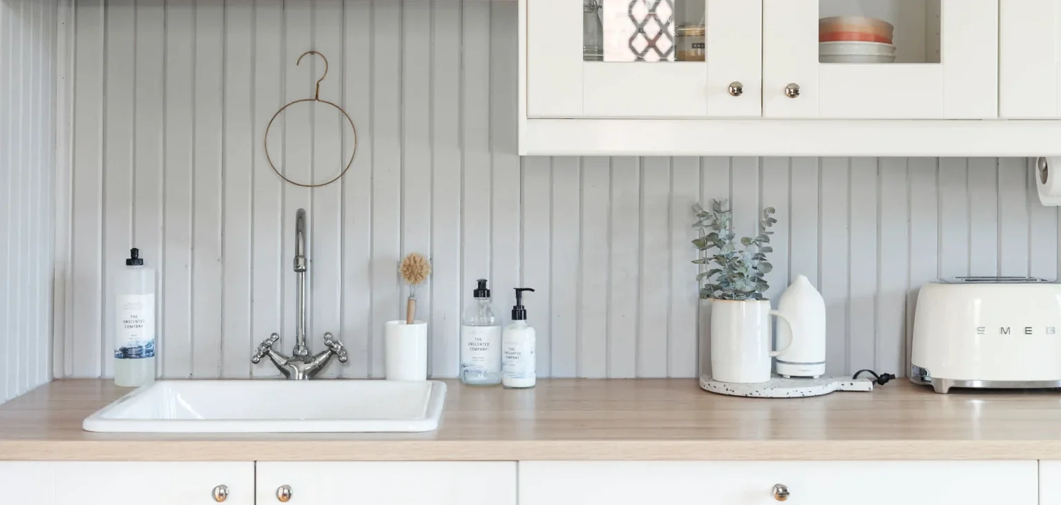 Soap bottles and a white brush holder stand beside a white kitchen sink on a wood-toned counter.