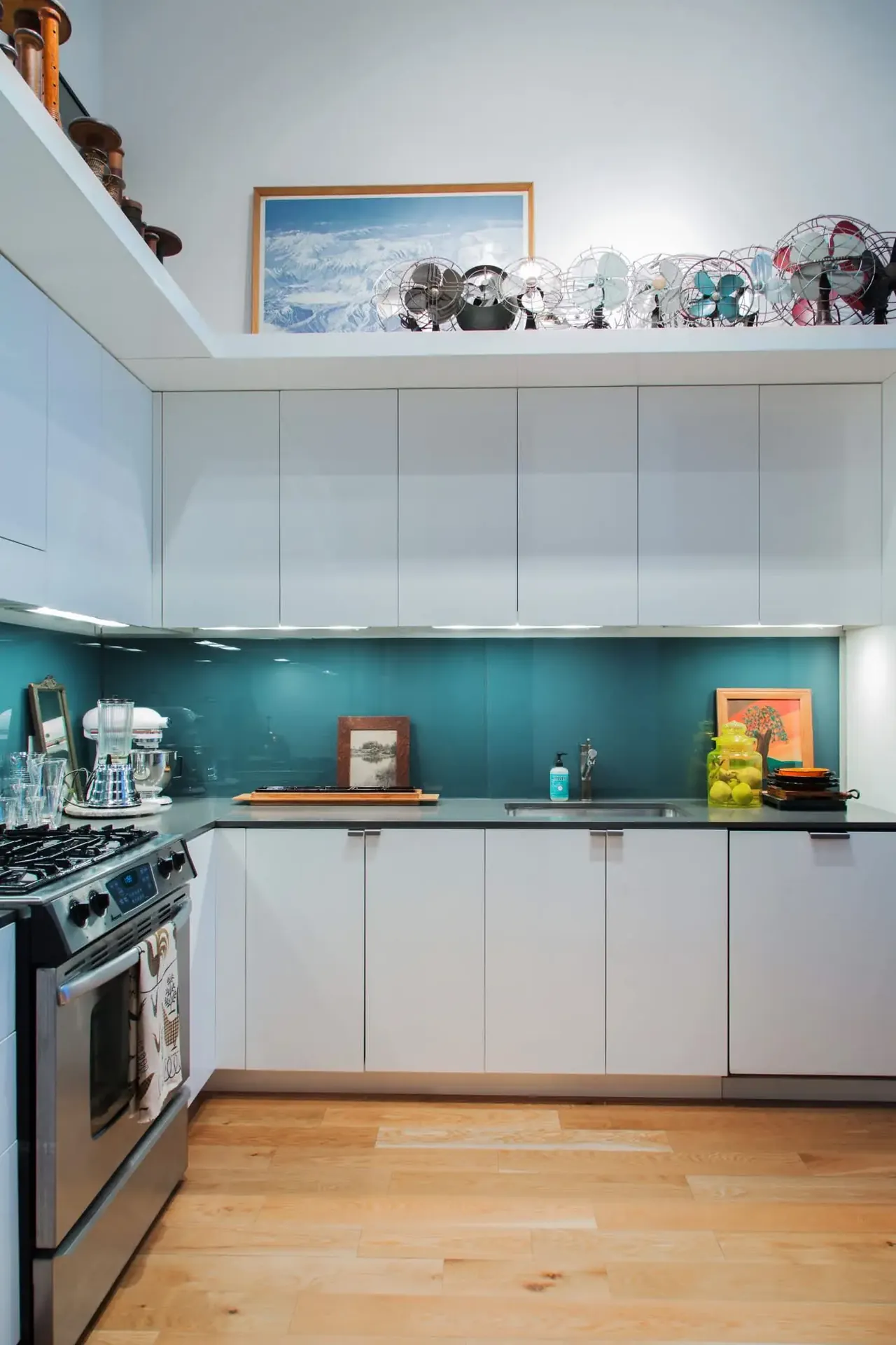 A small framed picture rests on a long tray against a teal kitchen backsplash.
