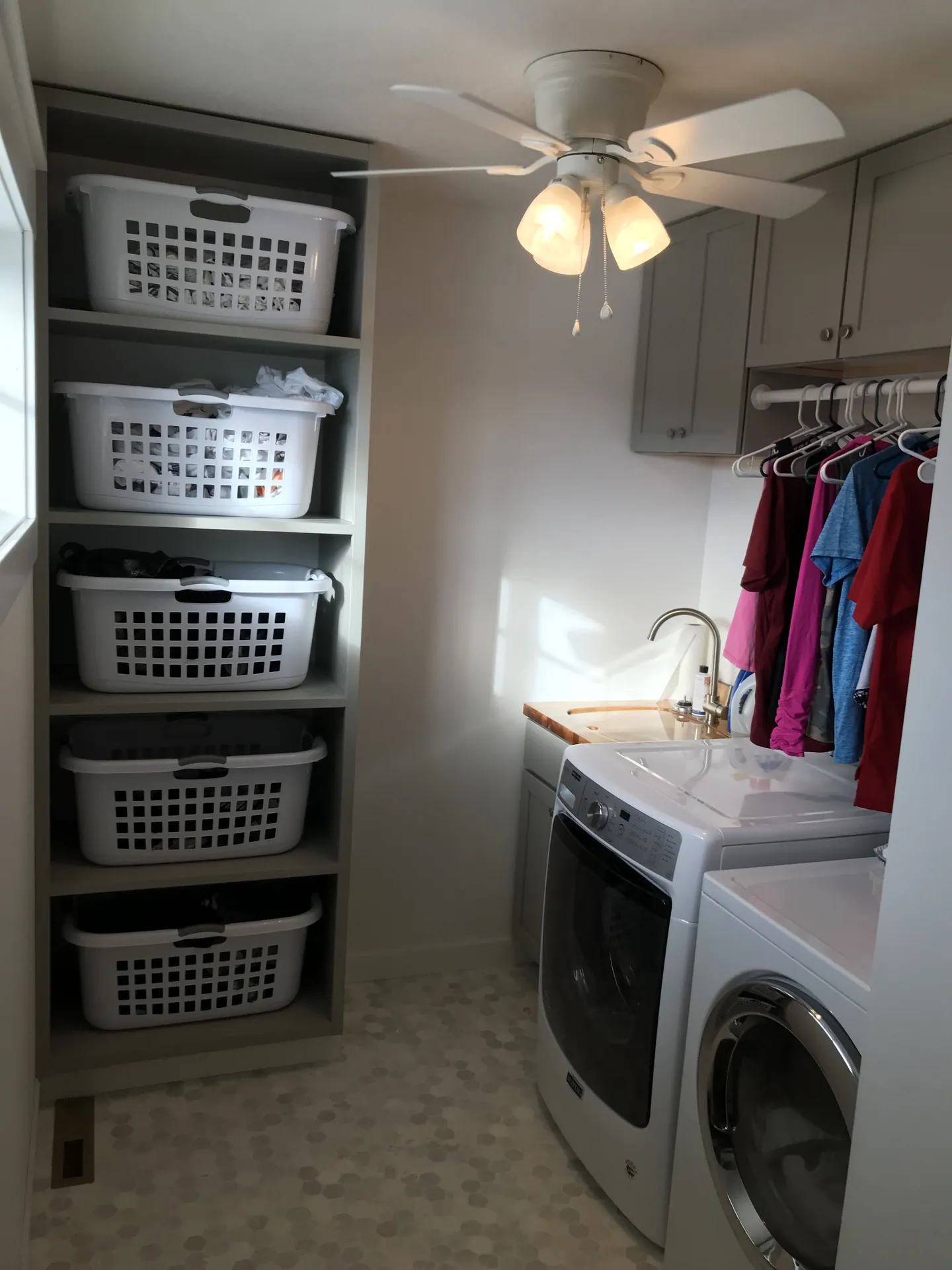White laundry baskets occupy separate shelves in a tall gray unit beside a washer and dryer.