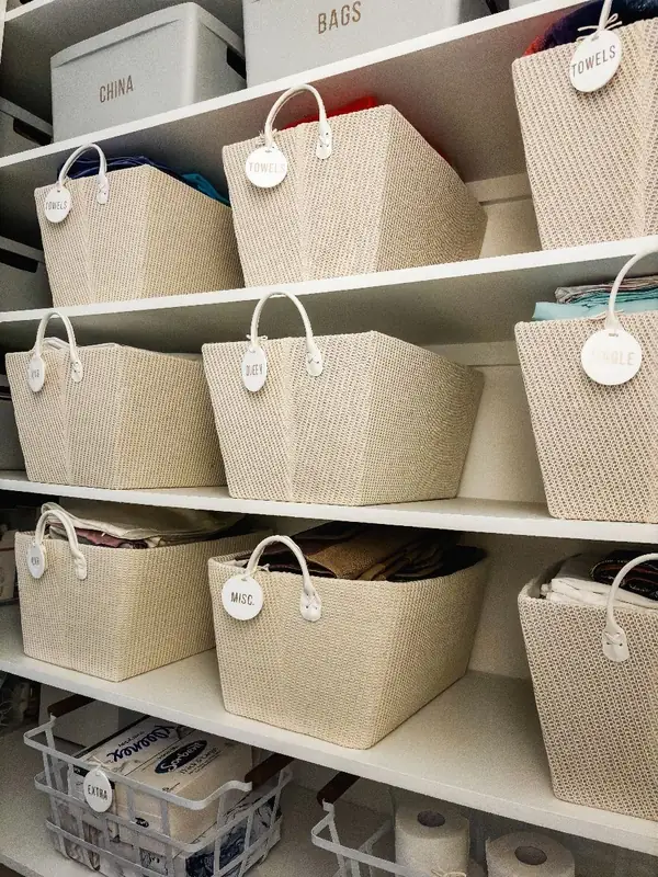 Cream baskets with round tags separating towels and bedding on closet shelves
