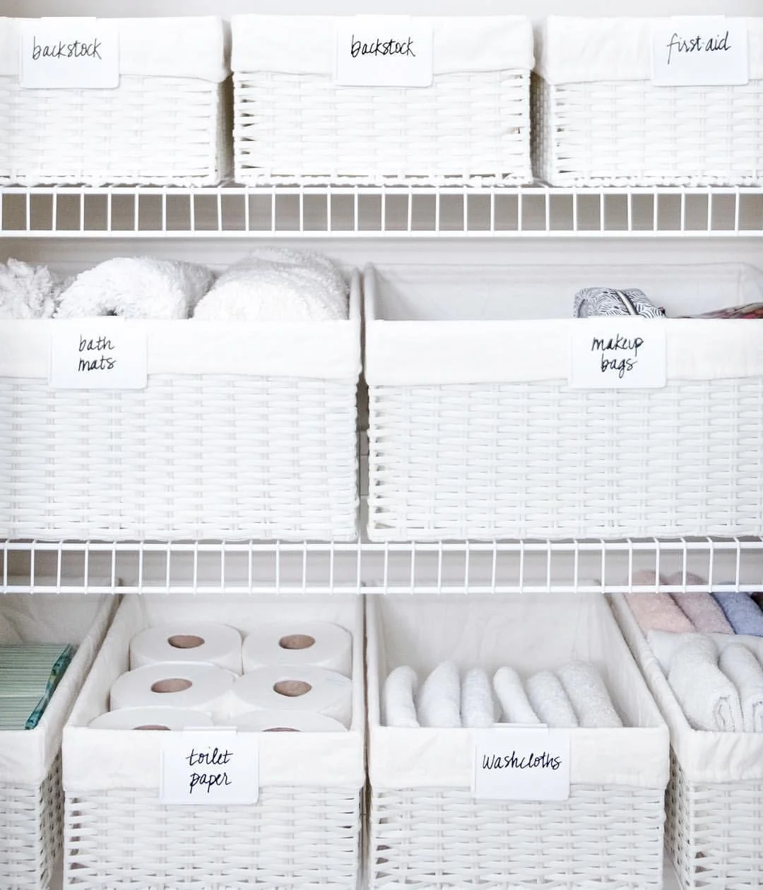 White labeled baskets on wire shelves, with rolled washcloths in a lower basket