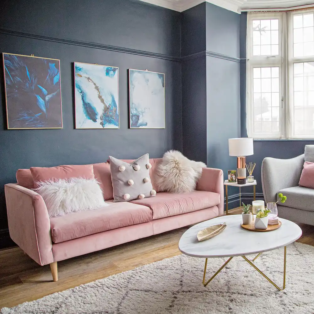 A pink sofa and cream rug sit against dark blue-gray walls with framed pictures.