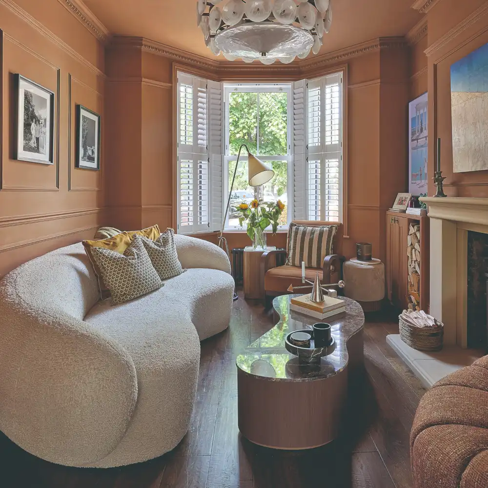 Terracotta walls surround a curved cream sofa with patterned cushions and a dark floor.