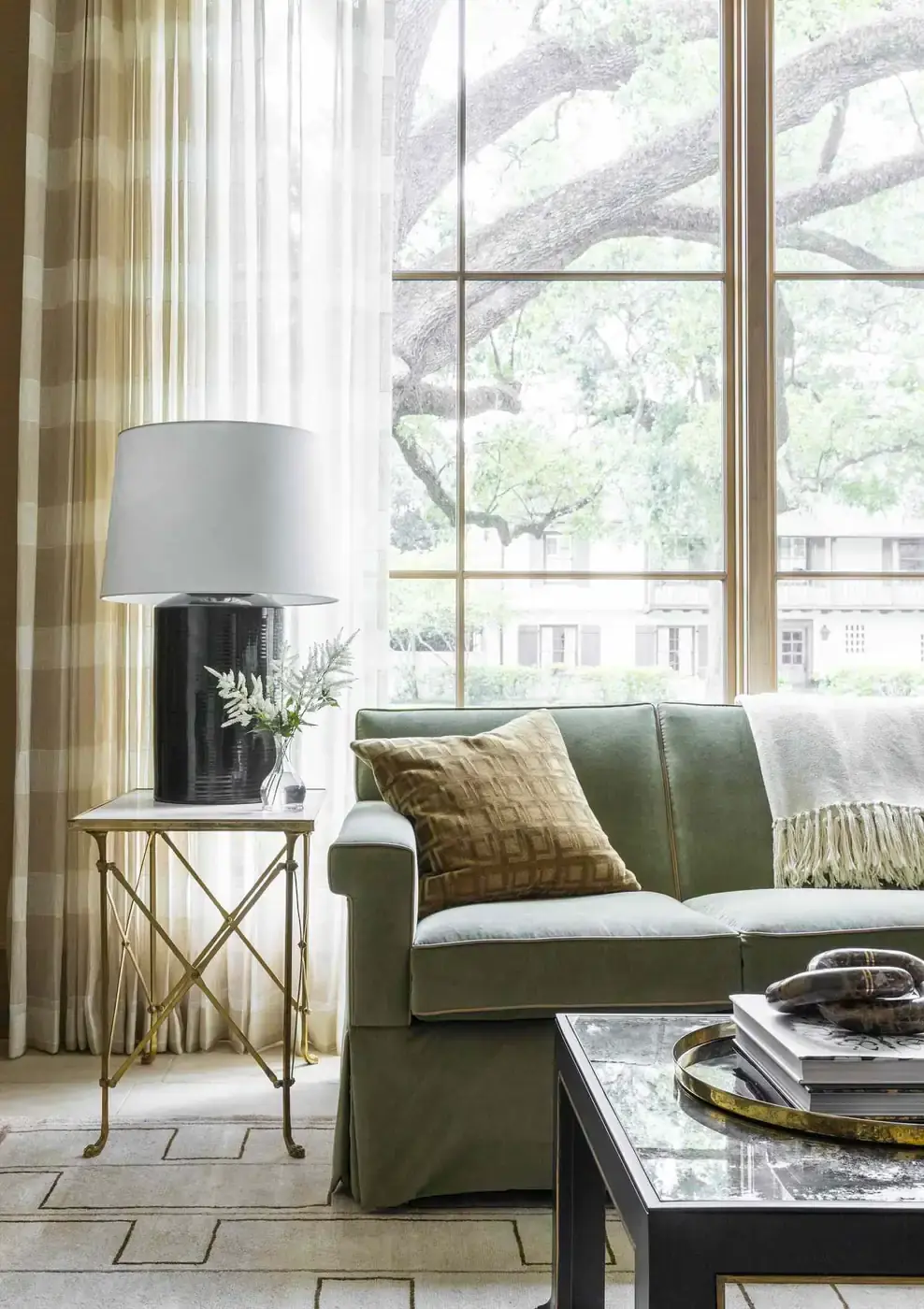 Pale checked curtains overlap white sheers beside a green sofa and a black table lamp.