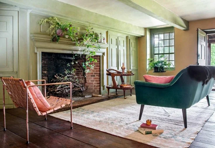 A teal chair faces a pink woven seat across a rug in a green paneled living room.