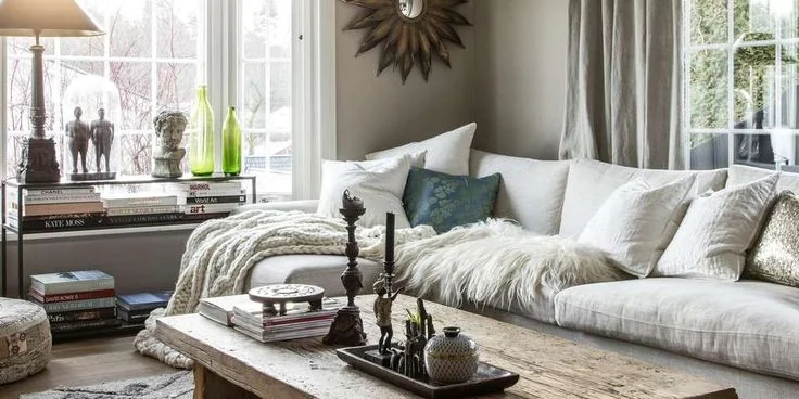 A pale sofa with light throws and a blue cushion sits beside windows and light curtains.