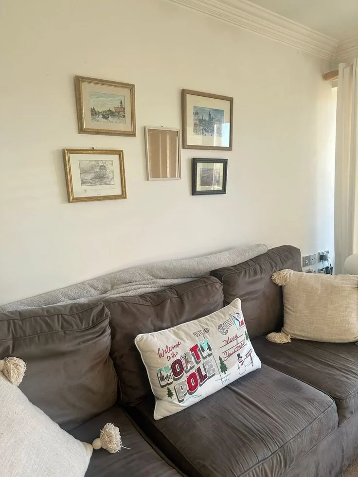 A small cluster of framed pictures hangs above a gray sofa on a pale wall.