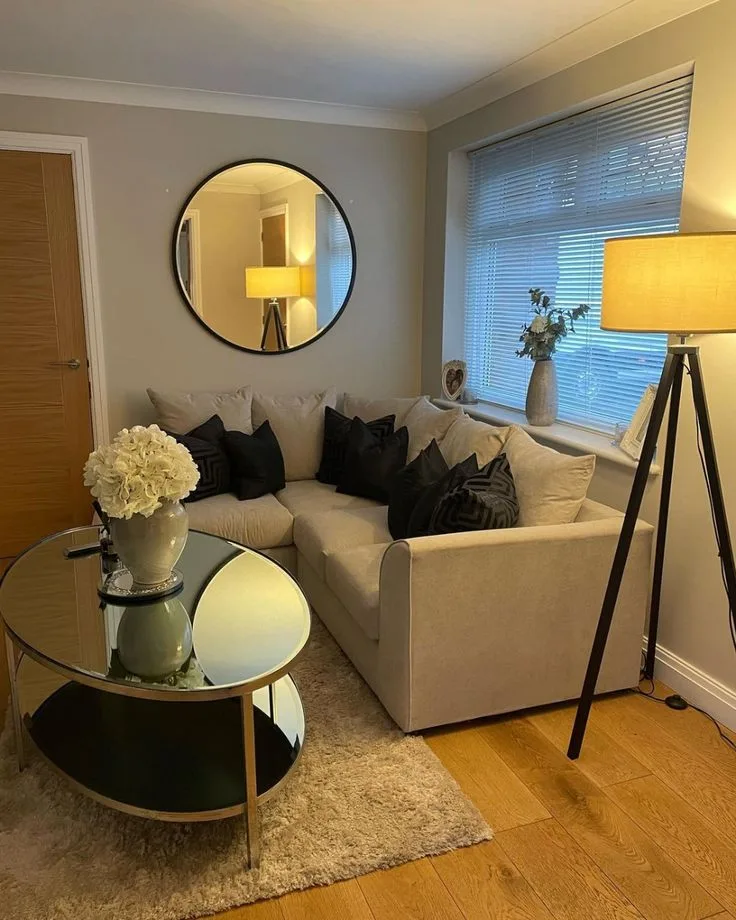 A large round mirror hangs above a pale corner sofa beside a floor lamp.