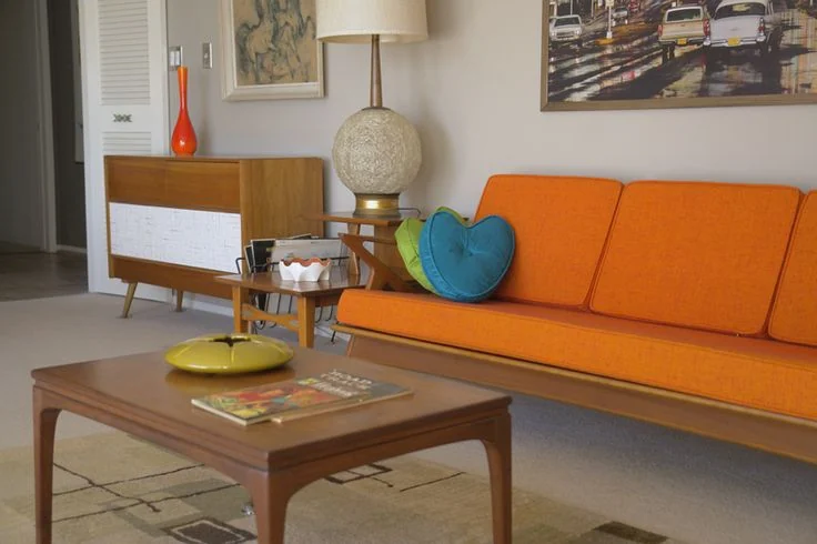 An orange straight-lined sofa stands beside a wooden cabinet and rectangular coffee table.