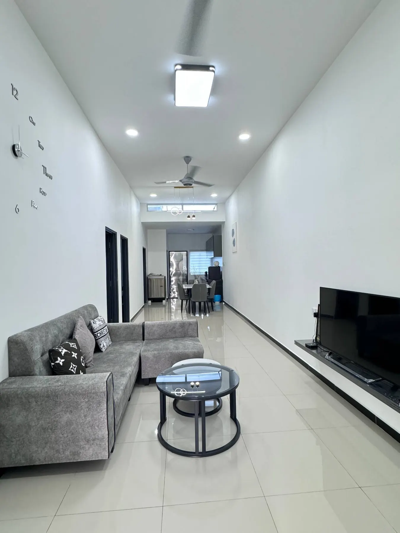 A gray sectional faces a TV on a floating shelf with a clear route toward a dining area.
