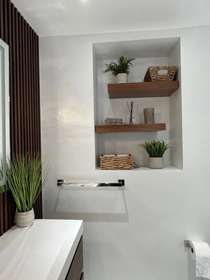 Wood-toned shelves inside a bathroom wall recess hold woven baskets, folded towels, and small planters.