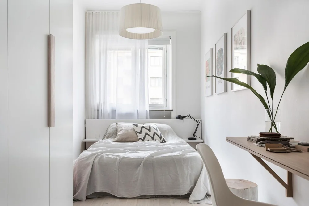 A bed sits beneath a window with a shallow desk along the side wall.