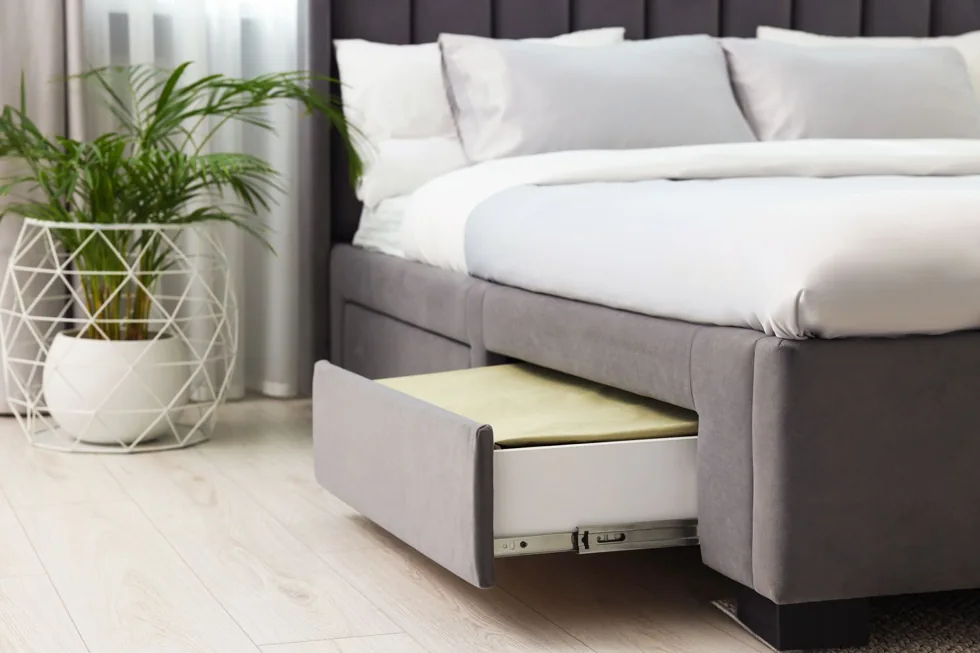 An upholstered bed has a partly open drawer with a pale item inside.