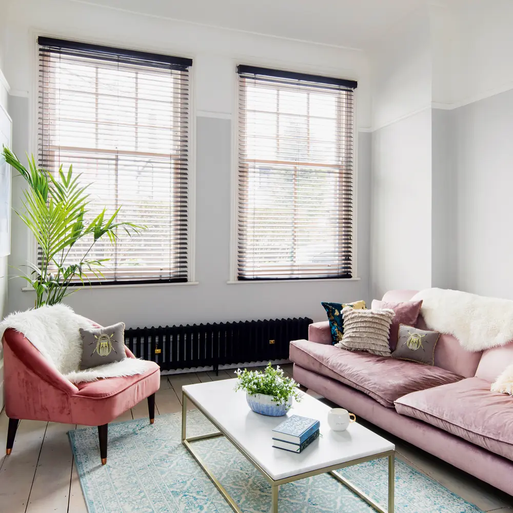 A pink sofa and separate chair sit at right angles beside two windows and a low table.