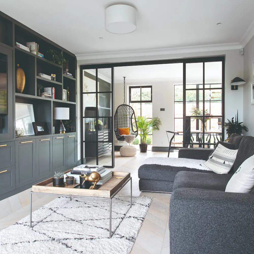 A gray chaise sofa faces a dark media wall beside a wide opening to another room.