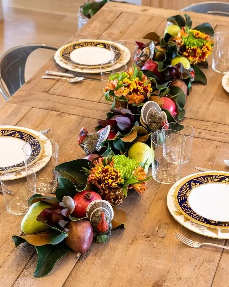 A leafy garland with fruit and small flowers runs along a wooden dining table.