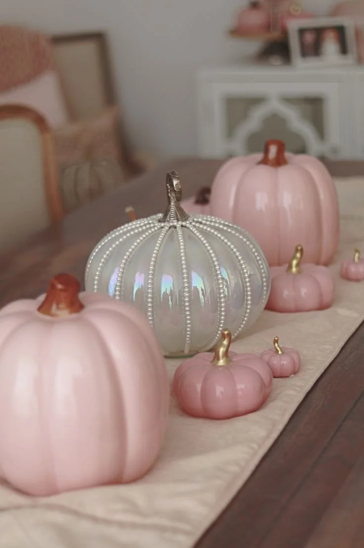 Pink pumpkins in several sizes sit on a pale runner across a dining table.