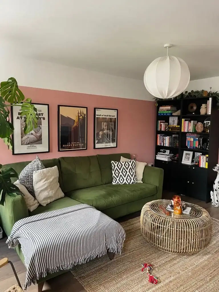 A green sectional against a pink wall with black and white pillows and a woven rug.