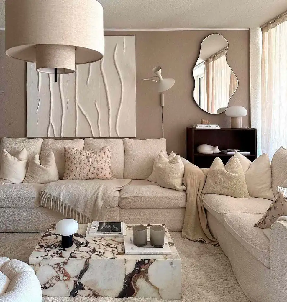 Cream sectional with small floral cushions beside a strongly veined stone-look coffee table against a taupe wall.